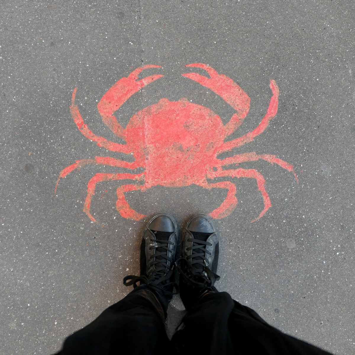 Pieds devant un graffiti de crabe rouge sur le sol