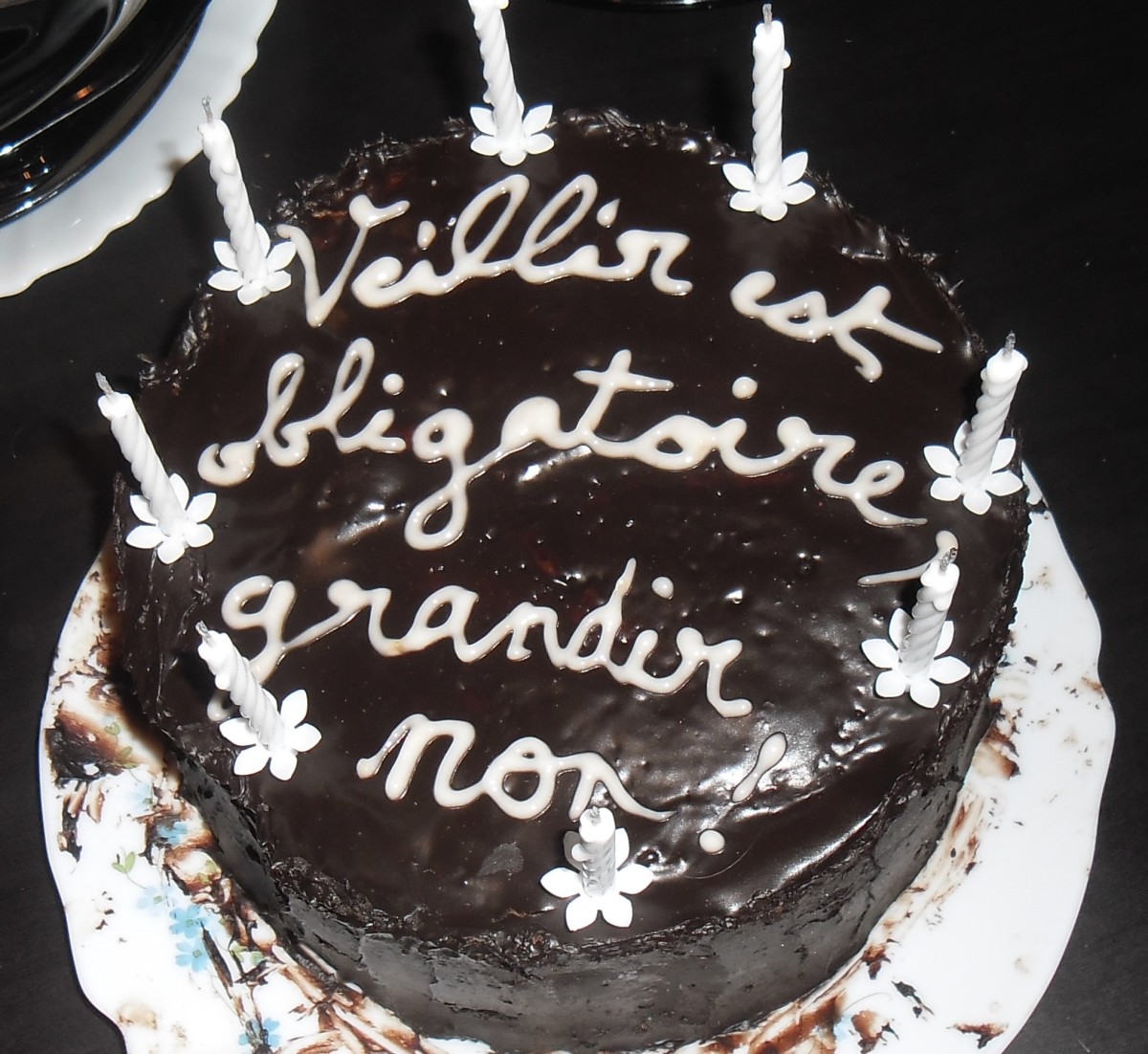 Un gâteau avec une ganache au chocolat et des bougies pour l'anniversaire de Florian avec écrit : "Vieillir est obligatoire, grandir non !"