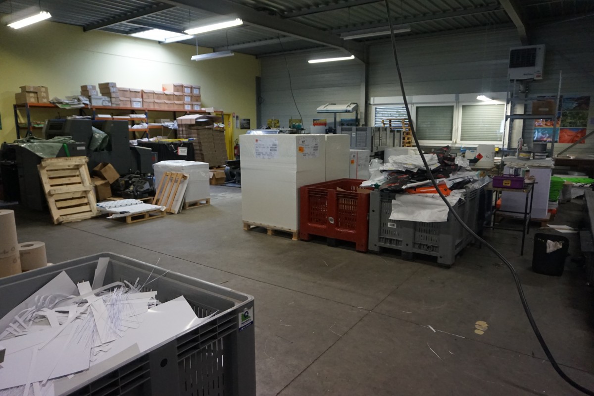 Dans l'imprimerie, on voit plusieurs gros bacs de déchets : papier, carton, emballages, ...