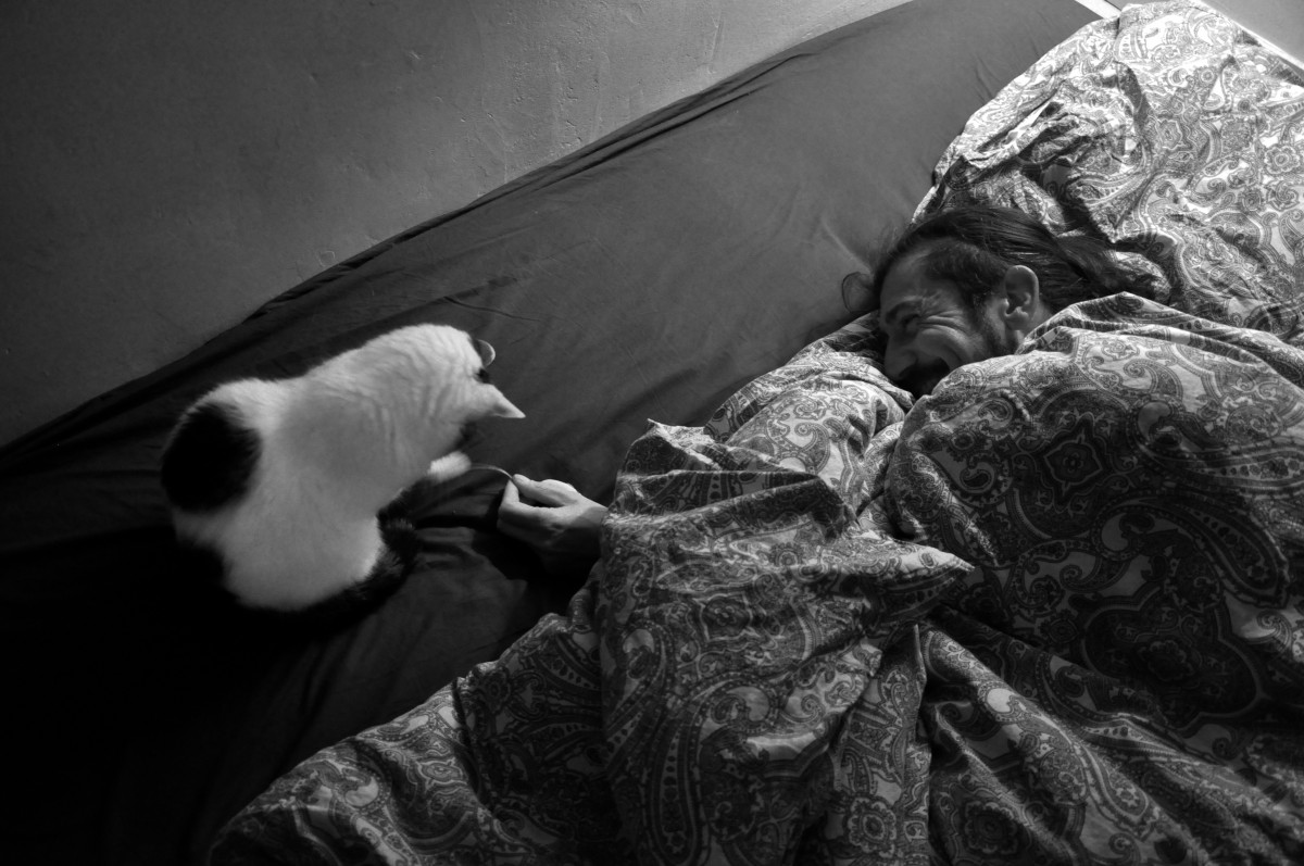 Homme allongé jouant avec un chat (noir et blanc)