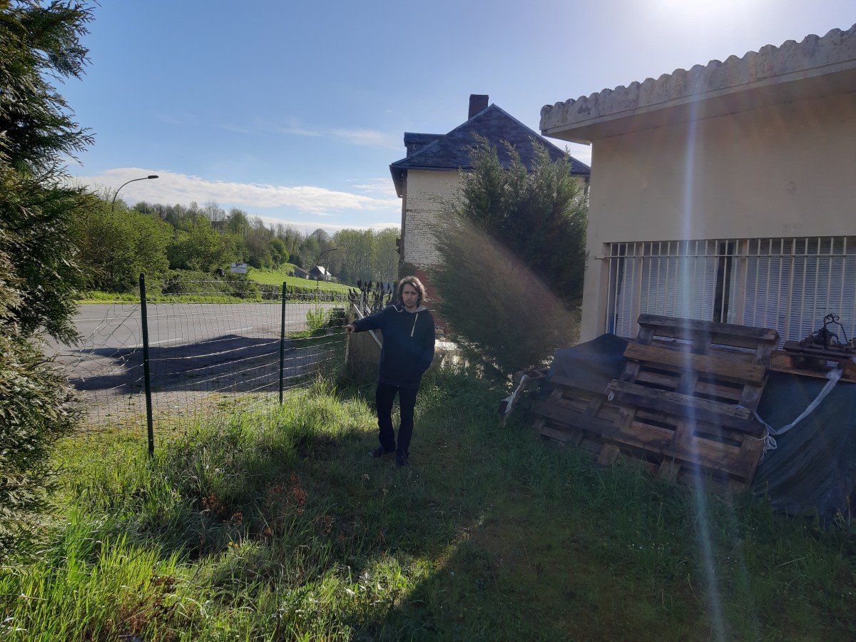 Florian au milieu entre la clôture qui donne sur la route et un petit batiment