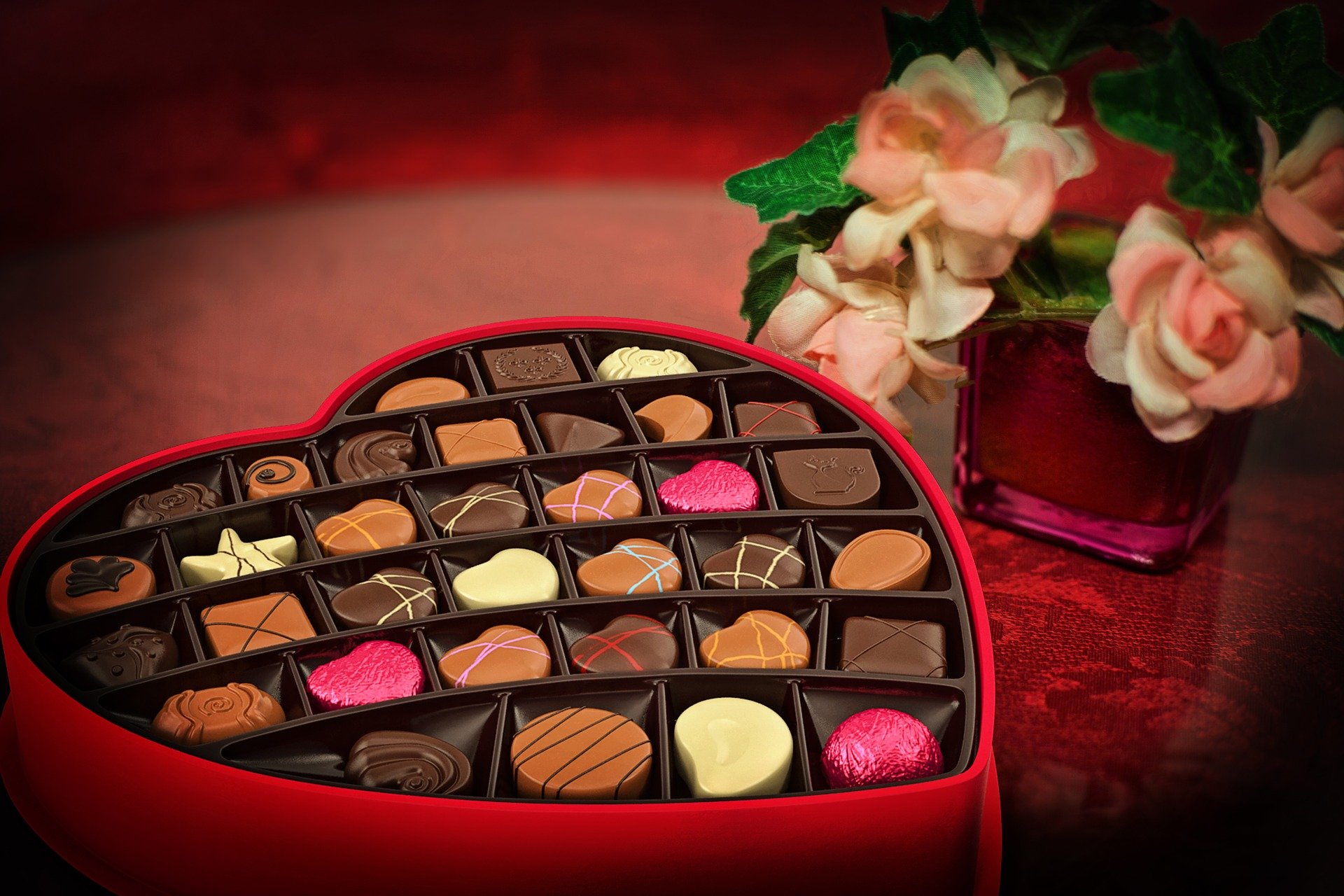 Boîte de chocolats en forme de coeur rouge avec des fleurs dans un vase à côté sur fond rouge