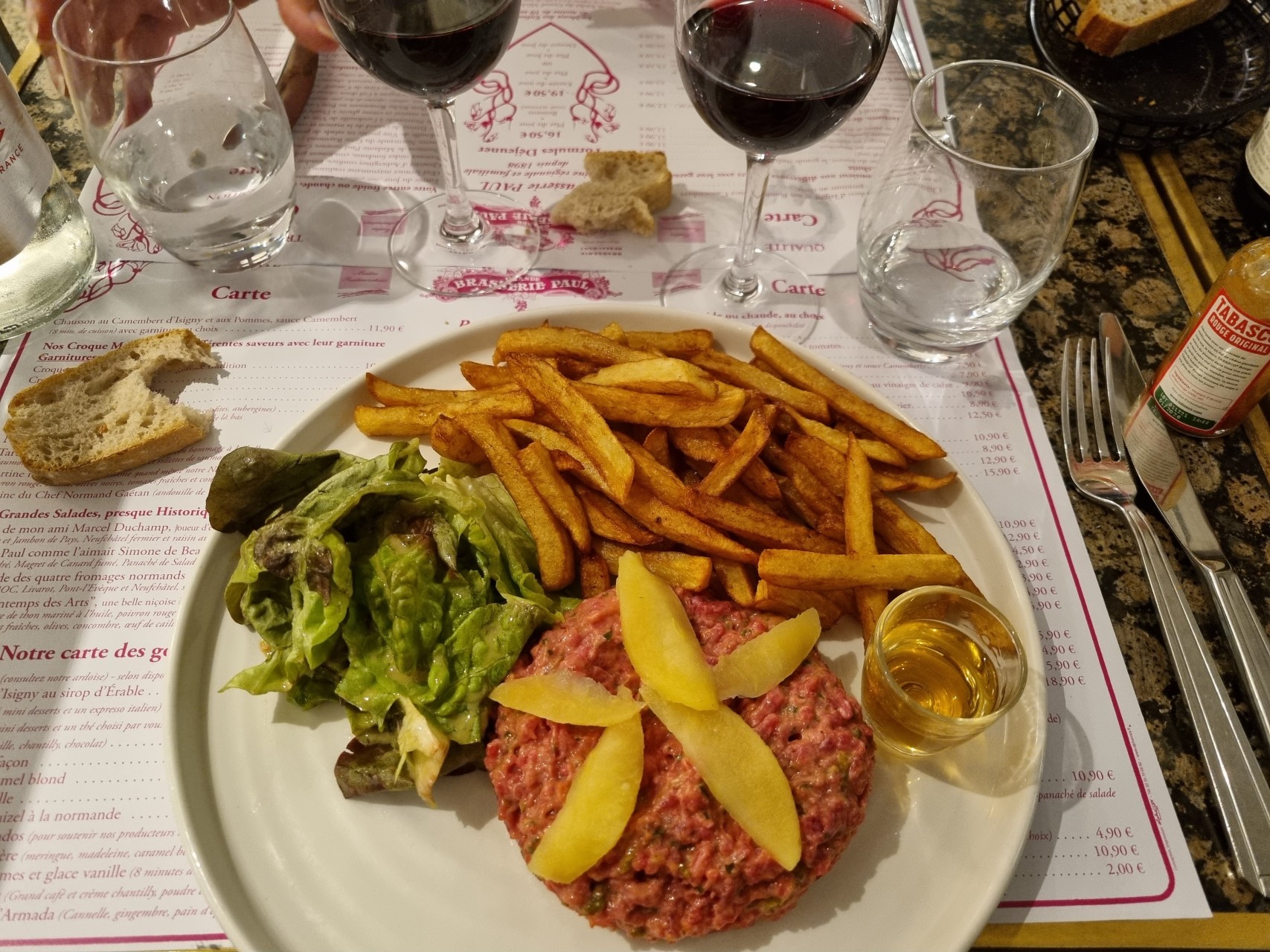 Assiette avec un steak tartare avec des pommes et un verre de Calvados accompagné de frites à la Brasserie Paul à Rouen
